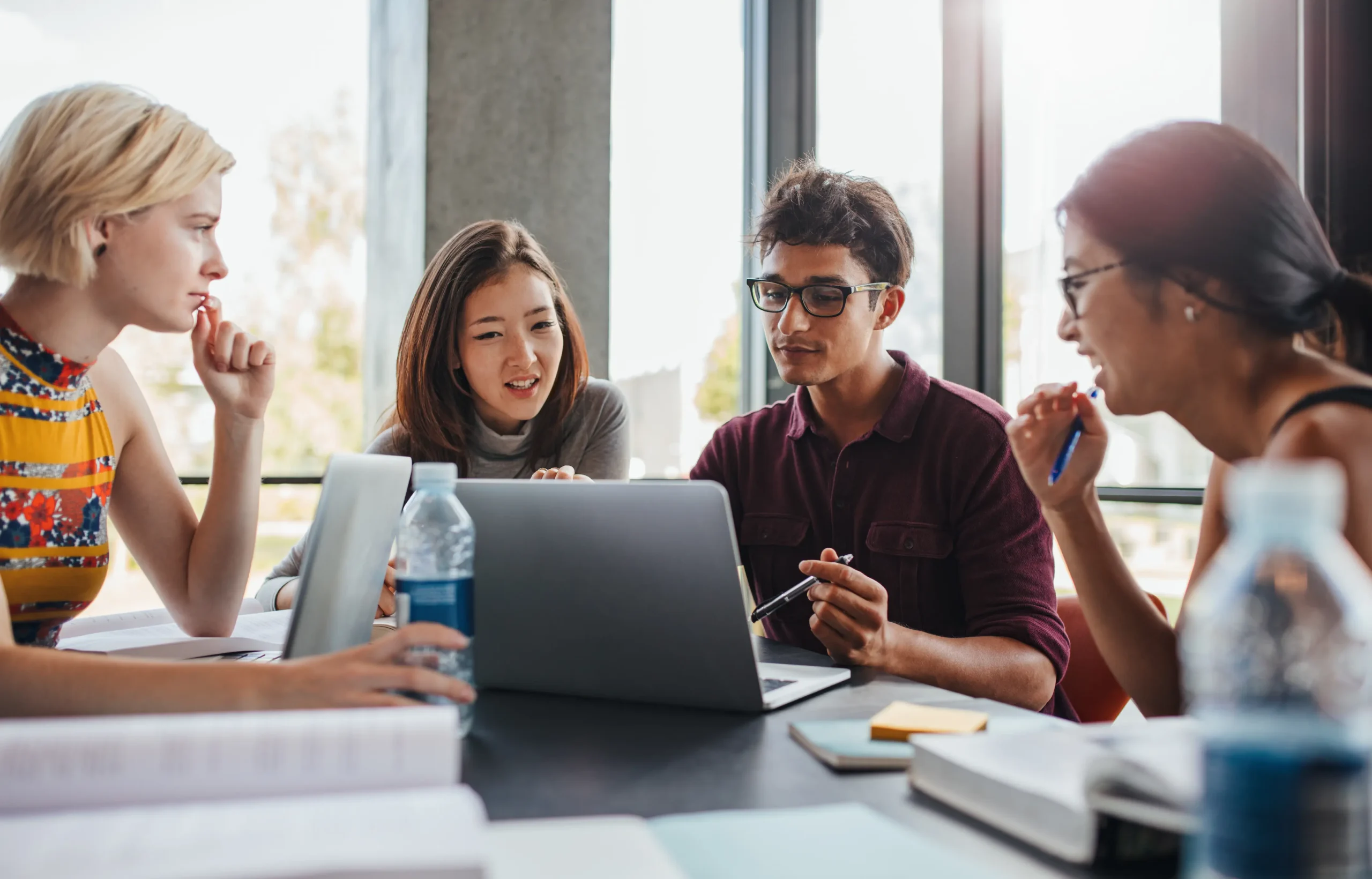 A group of young adults collaborating around a laptop in a bright room.