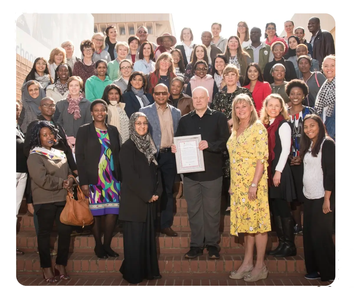 Large diverse group posing on stairs, some holding certificates.